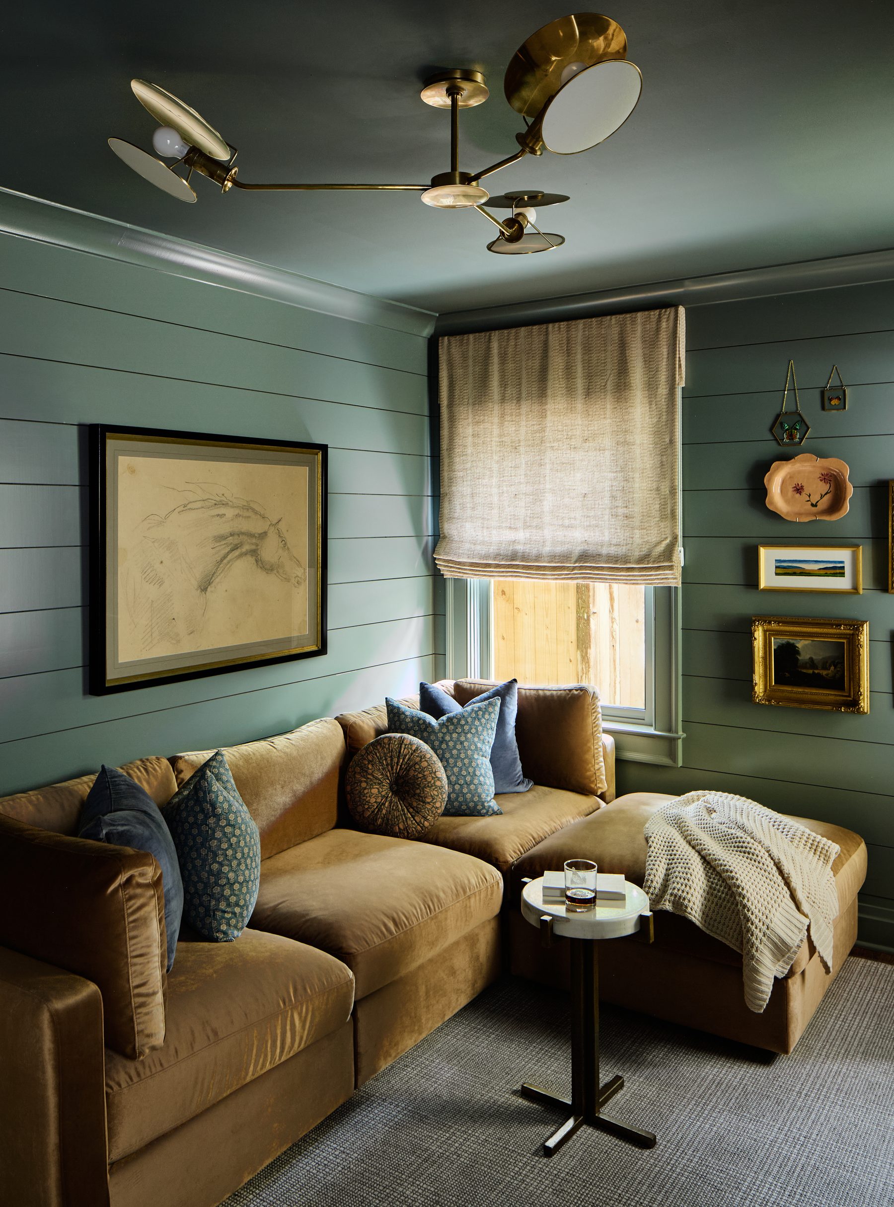 Cozy green den with velvet sectional sofa and brass sculptural lighting
