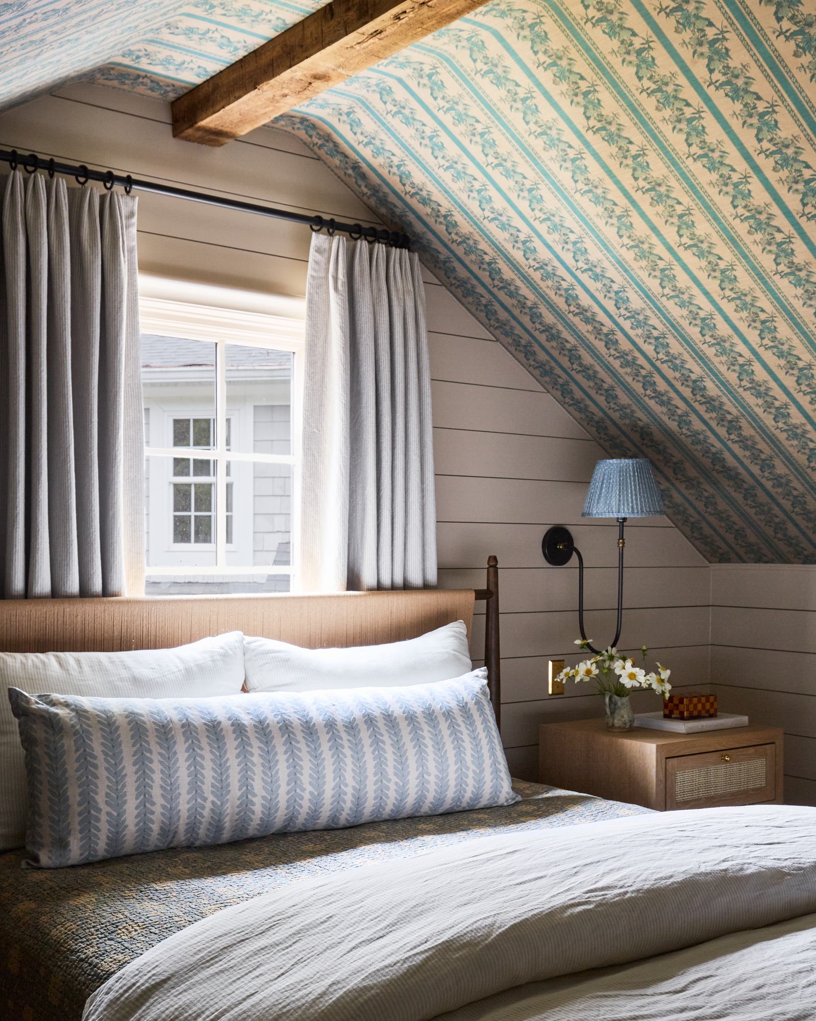 Attic primary bedroom with teal striped wallpaper, exposed wood beam, and pinch-pleat curtains