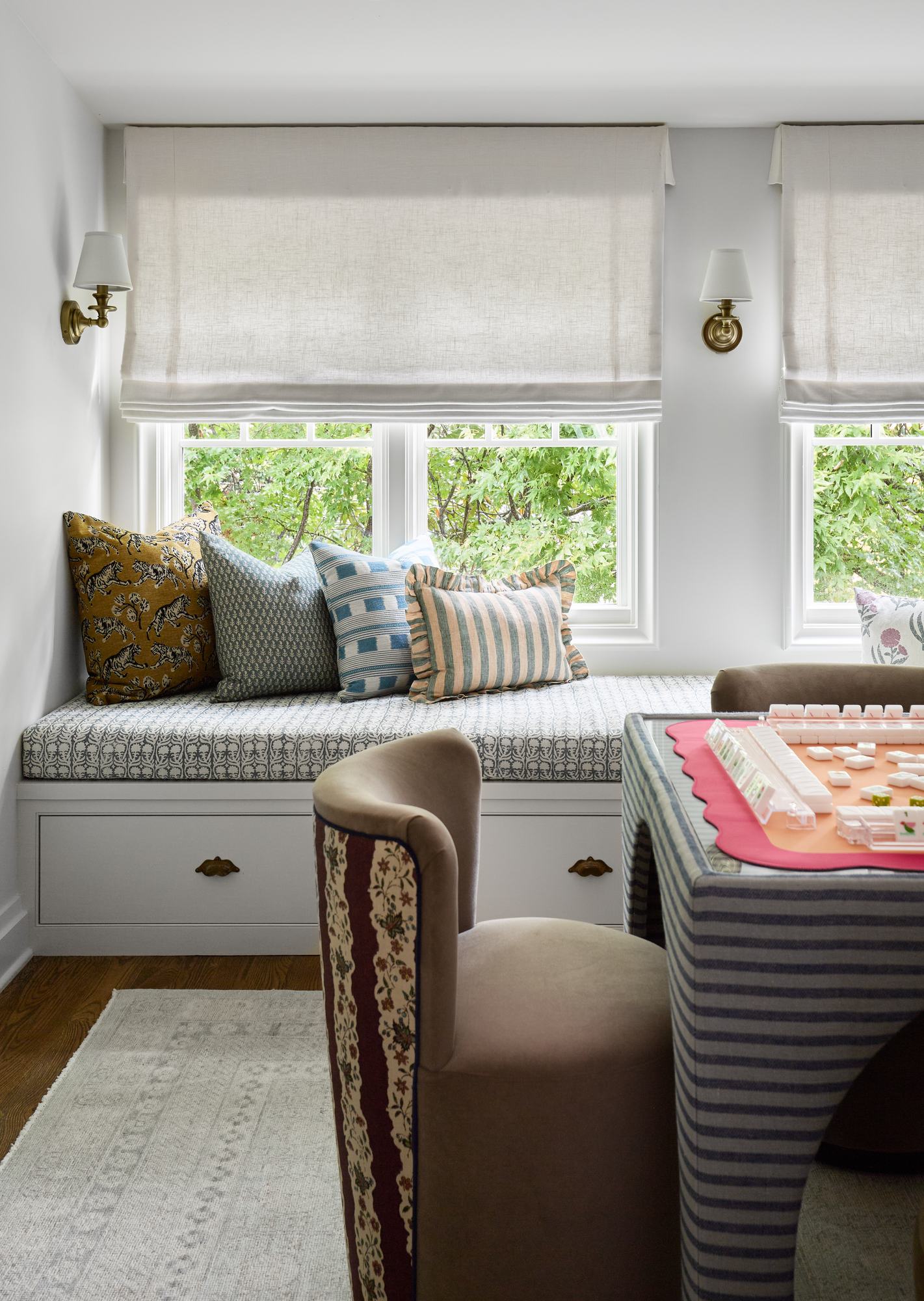 Built-in window seat with patterned cushion, mixed throw pillows, and a custom striped game table
