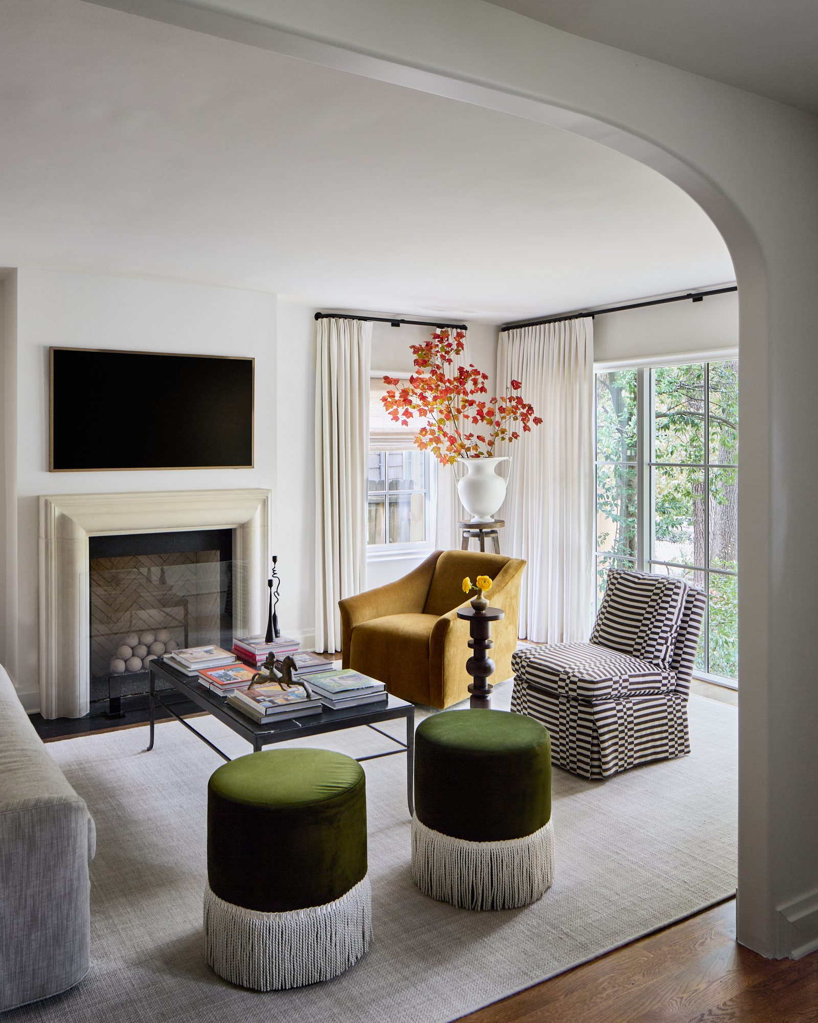 Living room with mustard velvet swivel chair, green fringe poufs, and stone fireplace