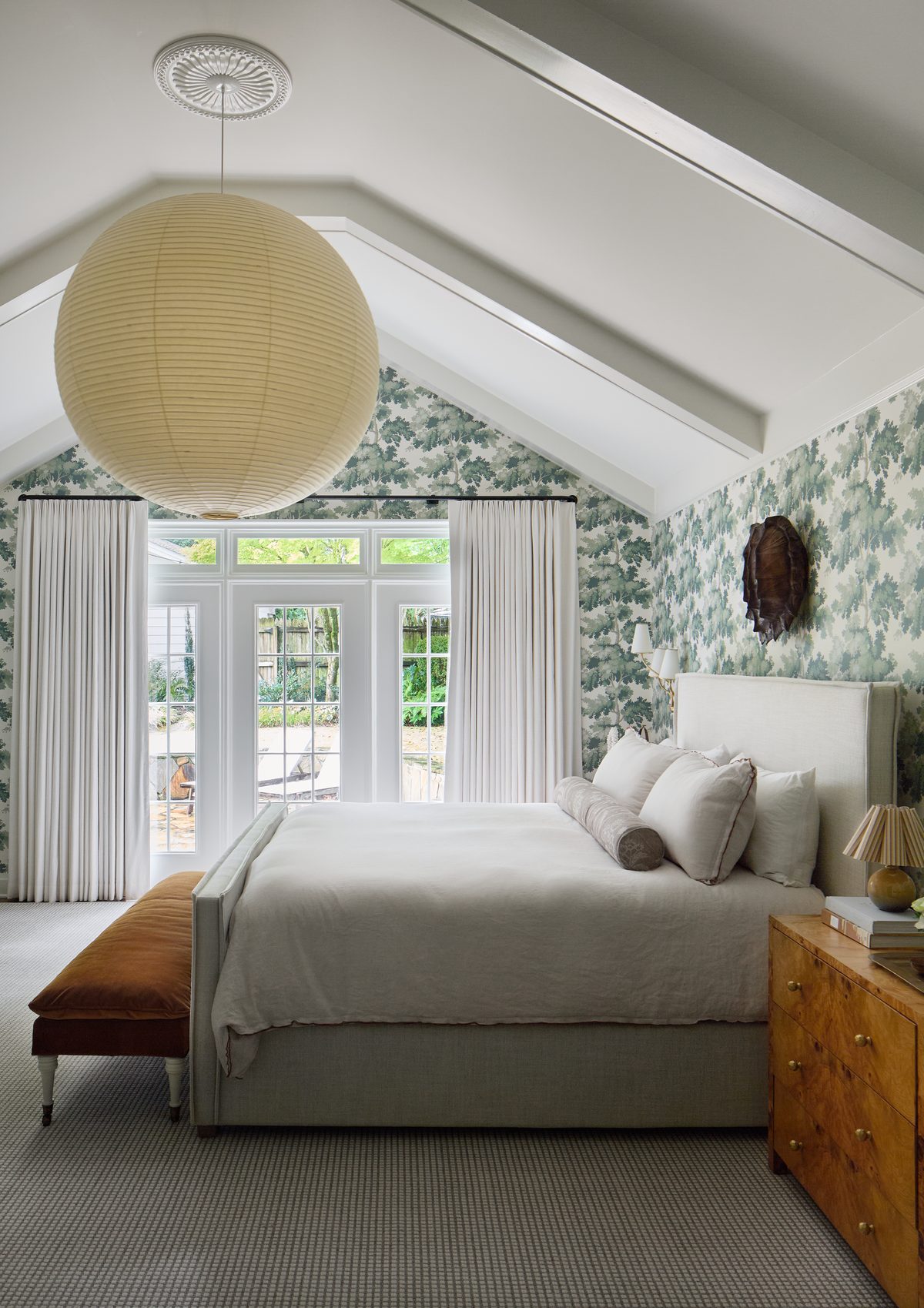 Vaulted primary bedroom with oak leaf wallpaper and paper lantern pendant